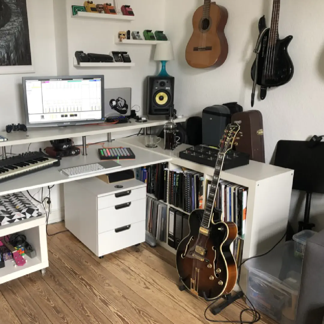 A desk with a computer, studio monitors, a MIDI keyboard, and a jazz guitar