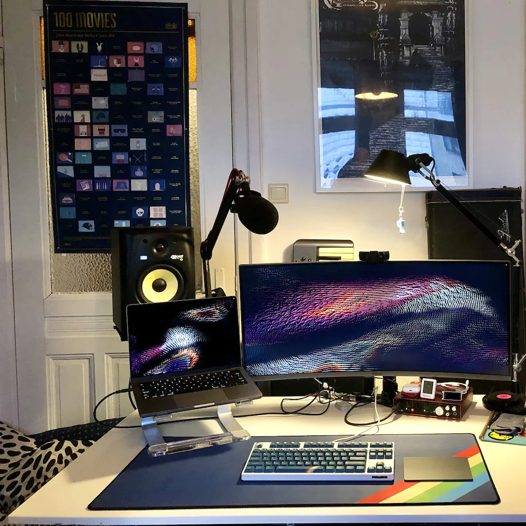 A desk with a computer, studio monitors, a wide screen monitor, mechanical keyboard and trackpad