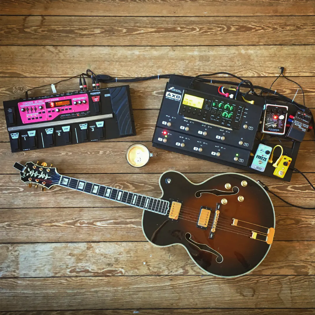 Top view of a cup of coffee, surrounded by my jazz guitar, a loop station and various other guitar effect pedals